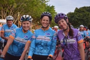 Three cyclists smiling at the start of the Cairns to Karumba Bike Ride, wearing C2K jerseys and helmets.